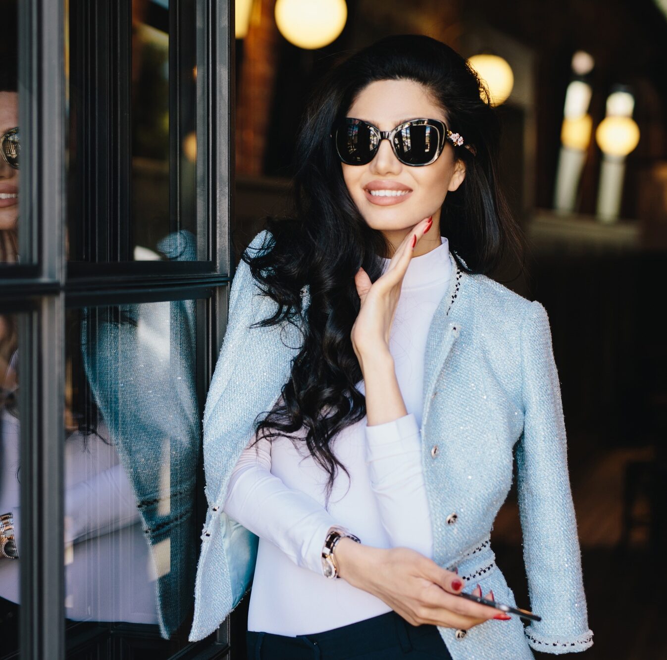 Glamour young woman with dark wavy hair wearing sunglasses and white blouse with elegant jacket